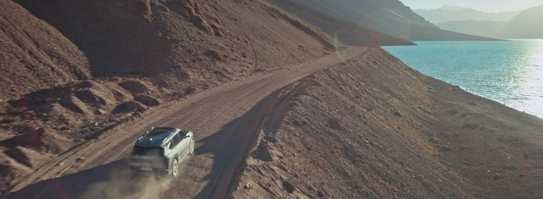 Kia Soundscapes, EV9 fährt alleine auf einer Straße durch wüstenähnliche Landschaft, Vogelperspektive