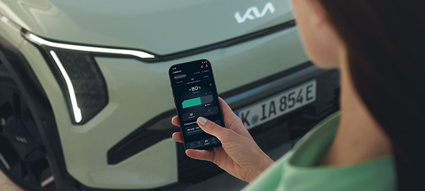 Frau mit Mobiltelefon vor Motorhaube, Display zeigt Kia-App