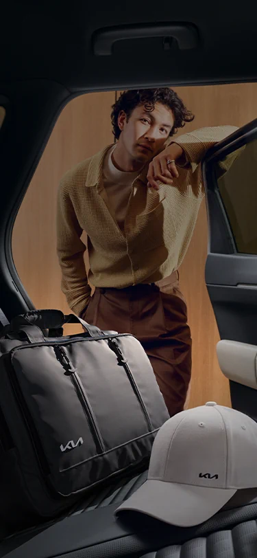 Ein Mann legt eine Kia Laptoptasche und eine Kia Sportkappe auf die Rücksitze seines Kia EV4.