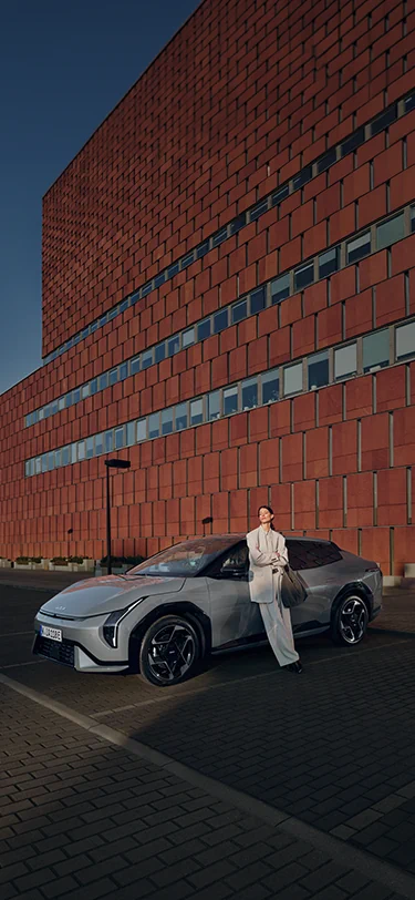 Eine Frau genießt die Sonne, während sie neben ihrem Kia EV4 steht.