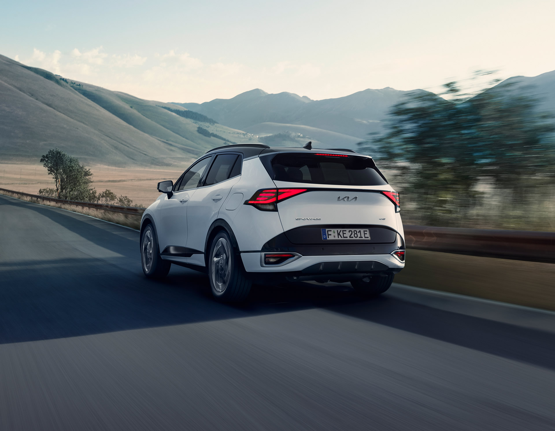 Kia Sportag PHEV, Heckansicht, Fahrt durch Landschaft