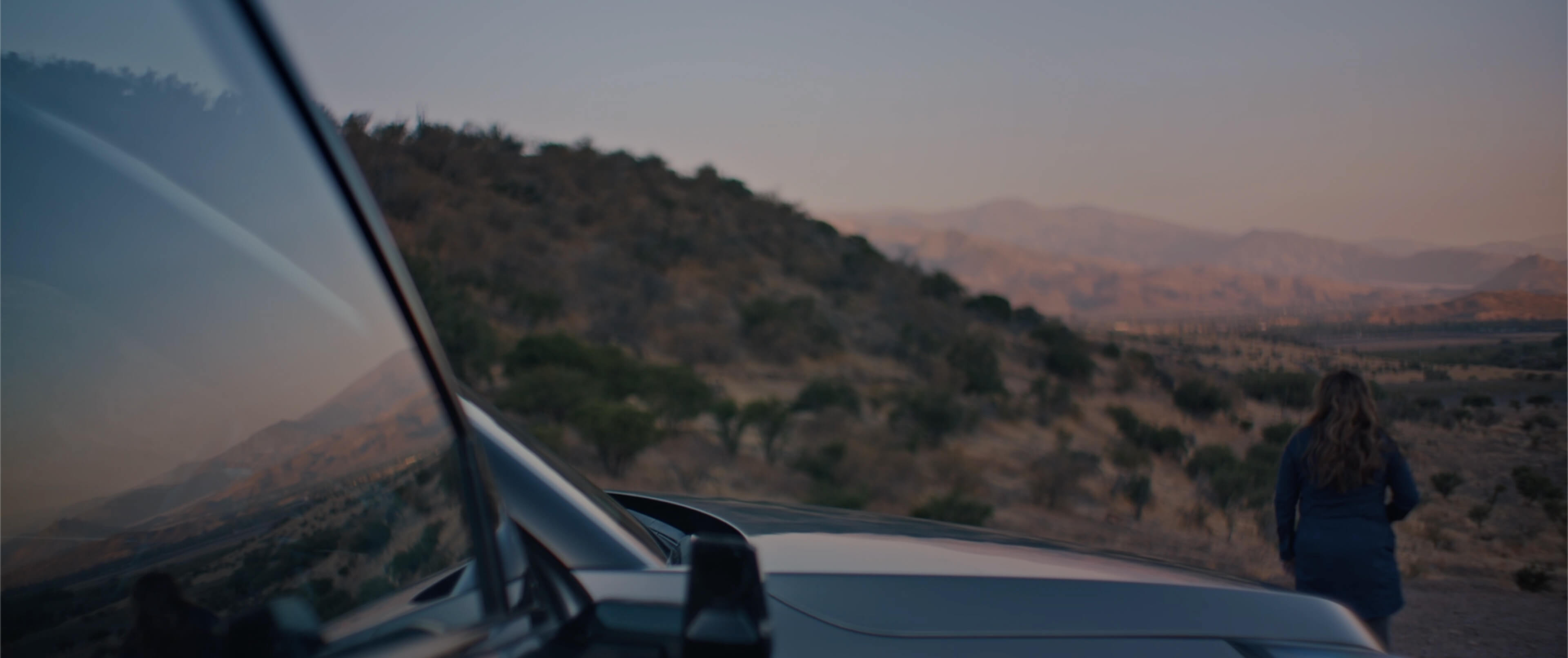 Kia Soundscapes. Anne steht vor dem EV9, der Landschaft zugewandt. Anklicken zum Starten des Soundtracks der auf Annes Roadtrip entstanden ist.