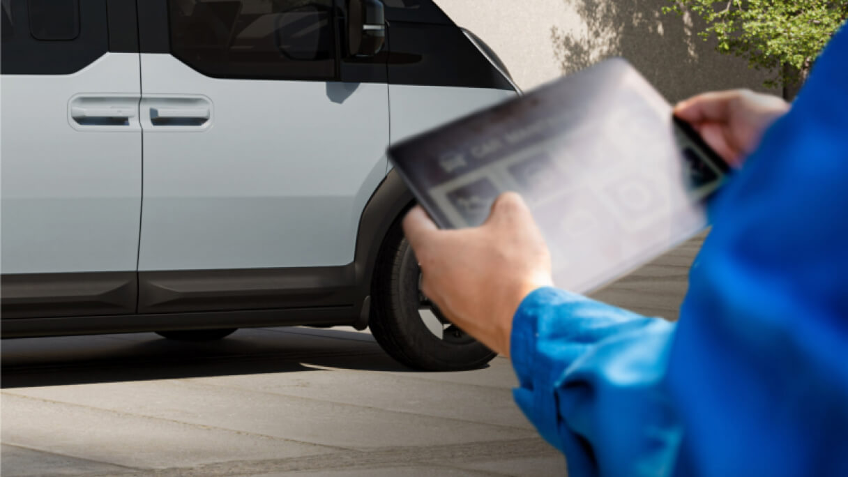 Primo piano di mani che utilizzano un dispositivo digitale vicino al motore di un veicolo, per mostrare l’accesso in tempo reale a Kia FMS (Fleet Management Solutions) e  ai Servizi dati