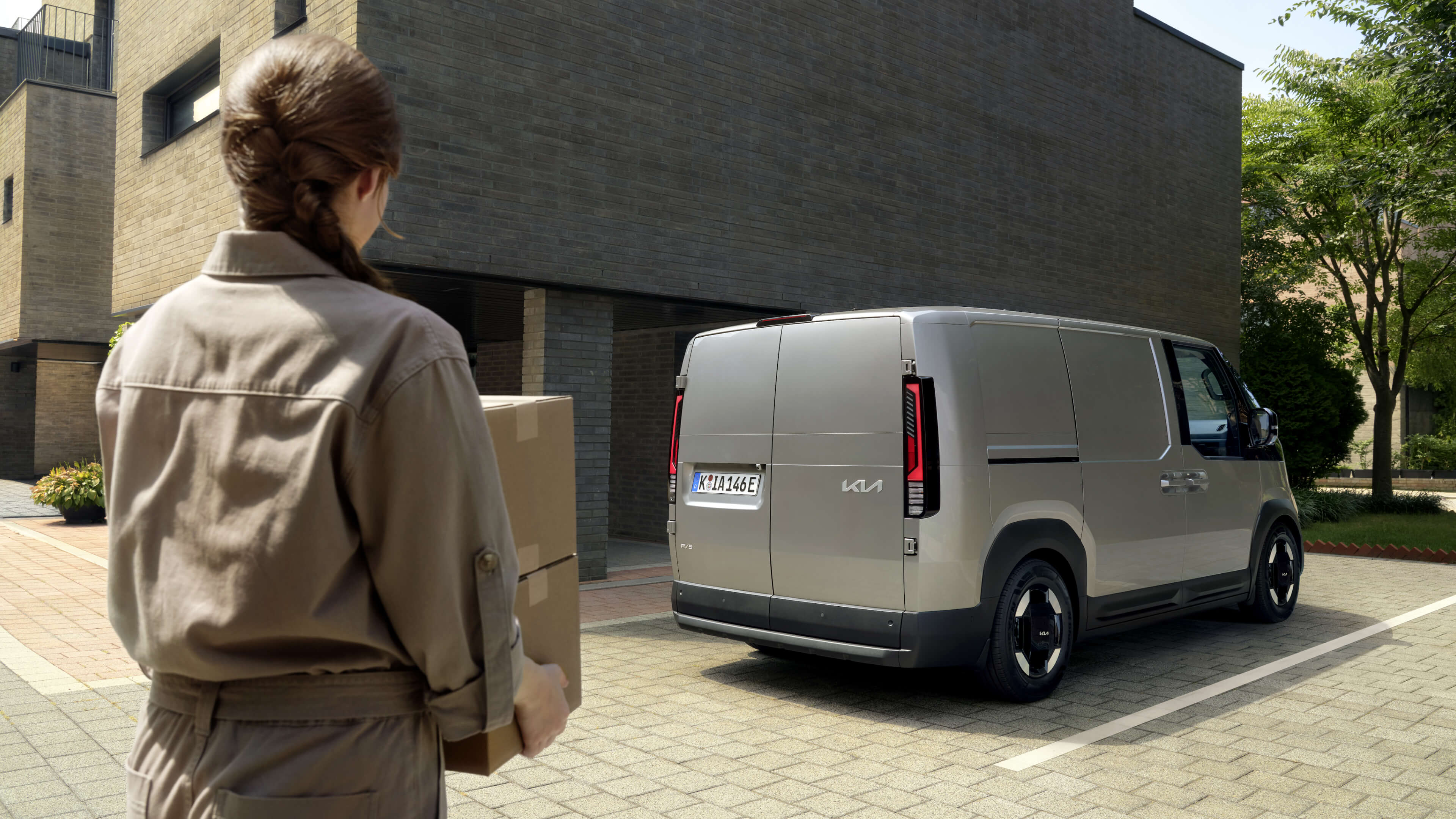 Eine Frau mit Paketen vor einem Kia PV5 in der Heckansicht.