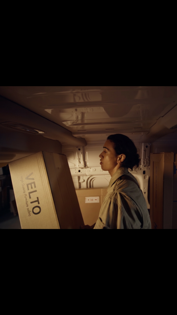 A person standing inside the tall cargo area of the Kia PV5 Cargo van, loading a large box among other packages