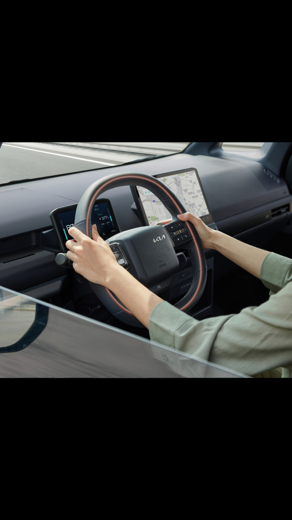 Close-up of the Kia PV5 Cargo steering wheel with driver’s hands