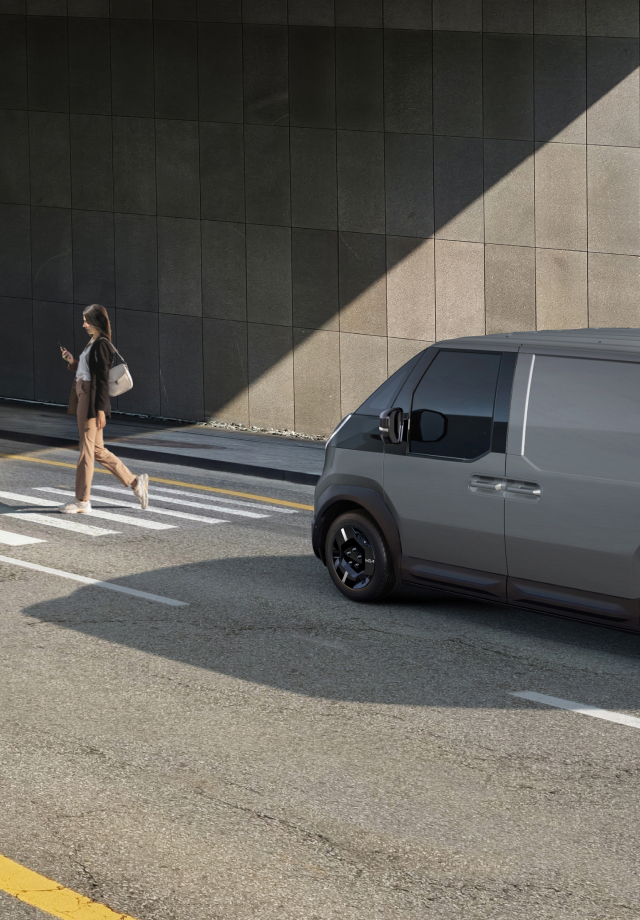 The Kia PV5 Cargo stopped at a crosswalk while a pedestrian walks by