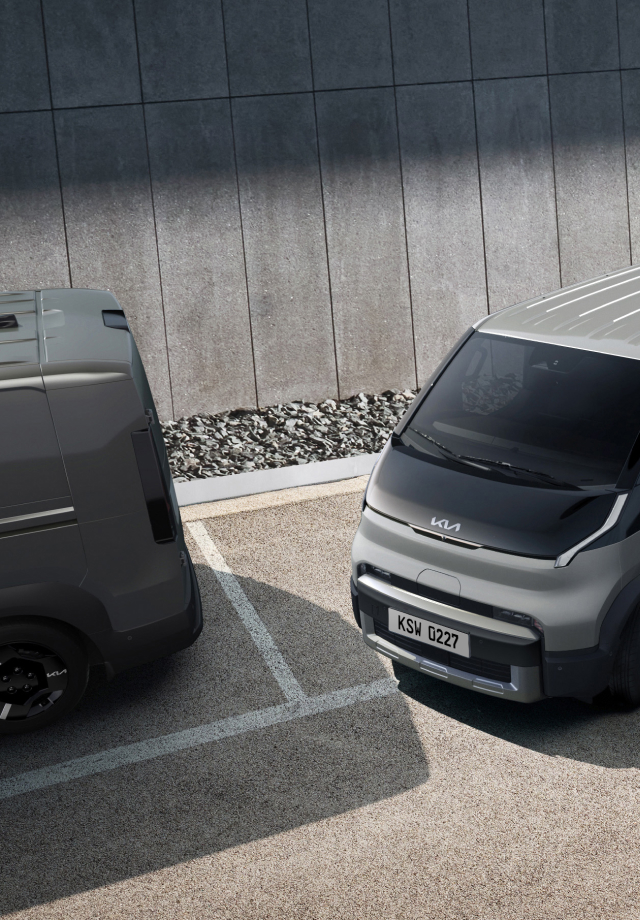 The Kia PV5 Cargo exiting a parallel parking space in a lot with two other vans
