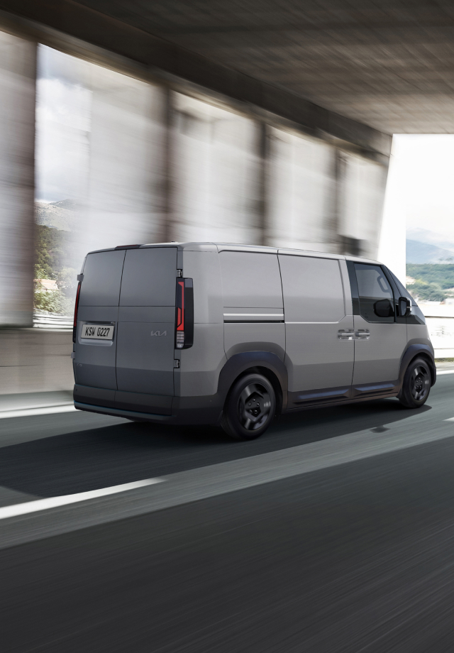 Rear view of the Kia PV5 Cargo driving on a highway with another van ahead