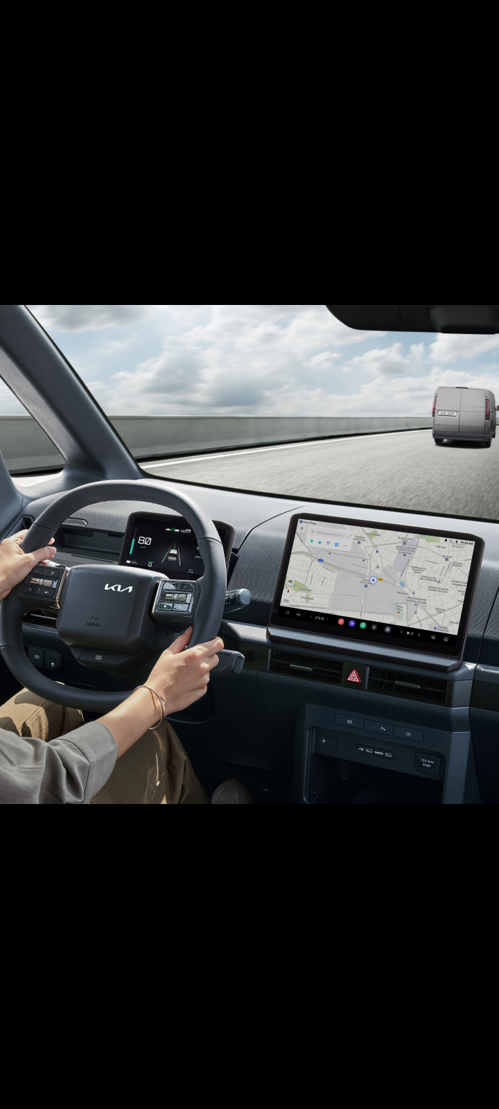 Driver holding steering wheel of the Kia PV5 Cargo with navigation screen visible