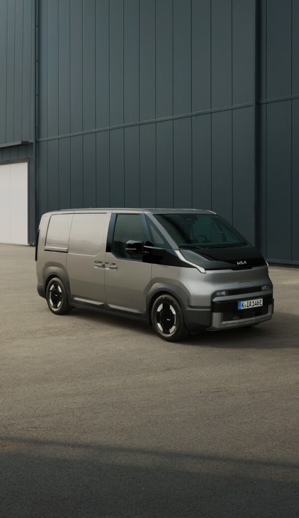 Rear view of the Kia PV5 Cargo charging with a man working on a laptop nearby