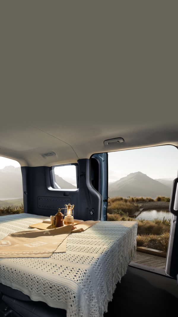 Interior of the Kia PV5 Passenger with the rear seats folded into a flat bed setup, overlooking a scenic landscape