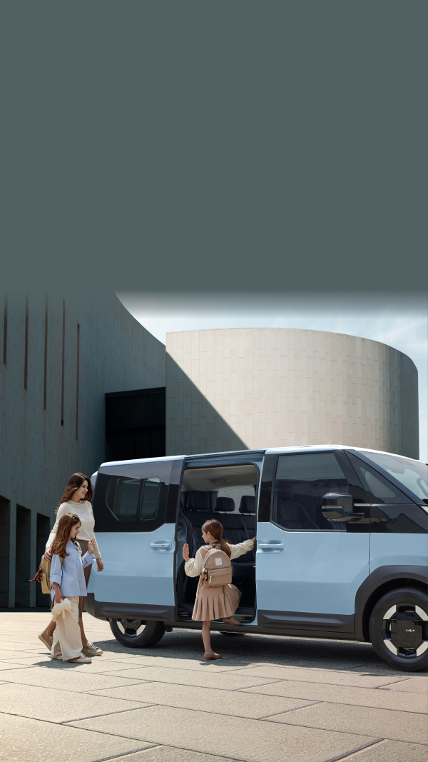 The Kia PV5 Passenger with dual sliding doors open, as a mother and children prepare to board