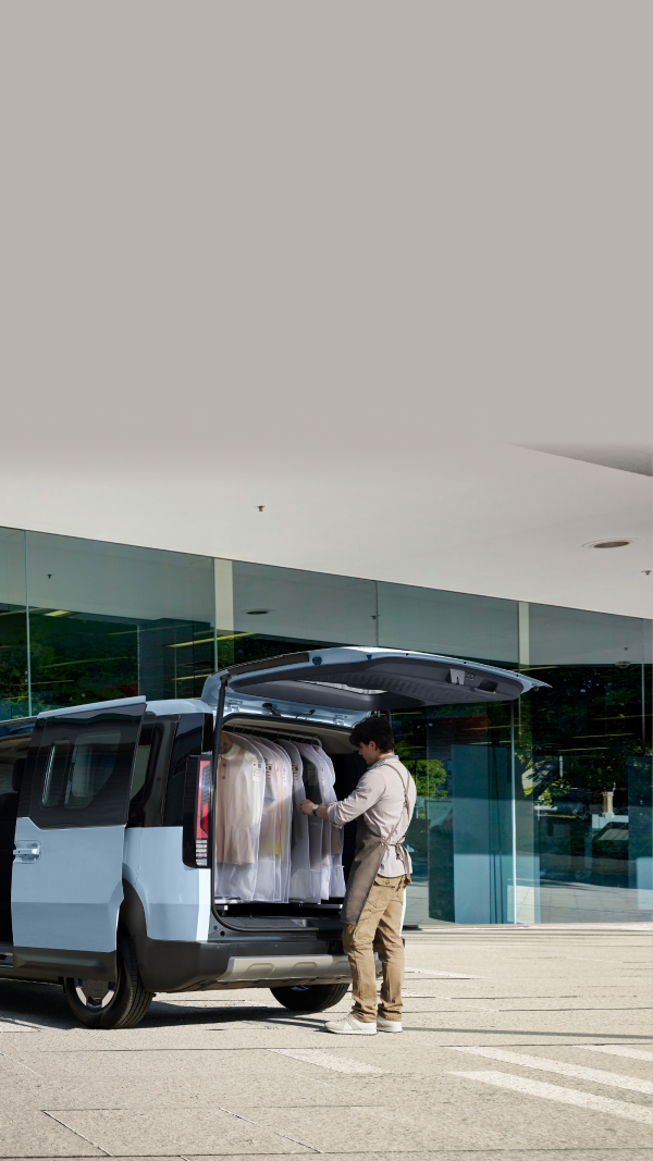 The Kia PV5 Passenger parked outside a laundromat with the rear door open, showing laundry being loaded and unloaded