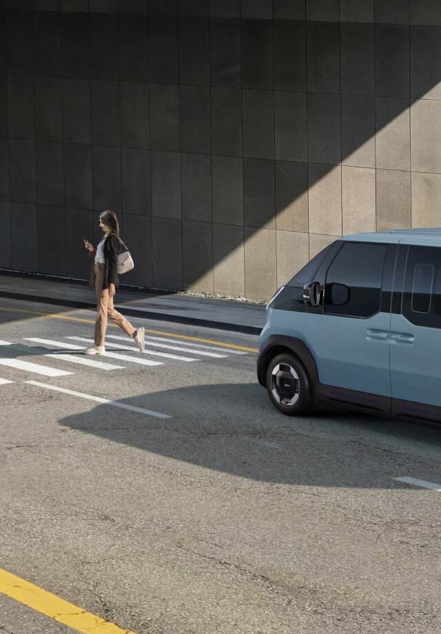 The Kia PV5 Passenger stopped at crosswalk while a pedestrian walks by