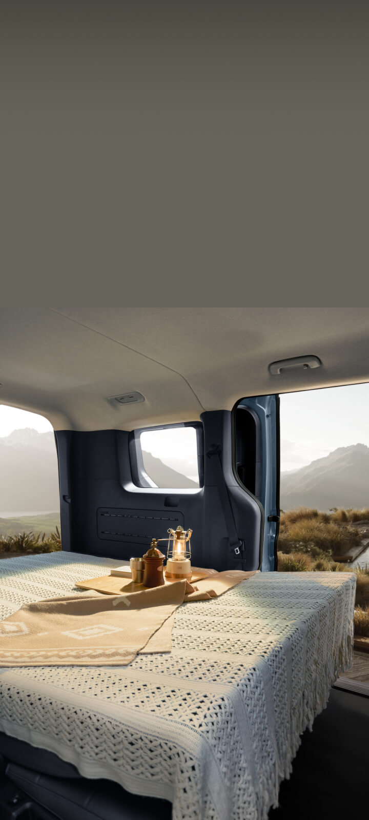 Interior of the Kia PV5 Passenger with the rear seats folded into a flat bed setup, overlooking a scenic landscape