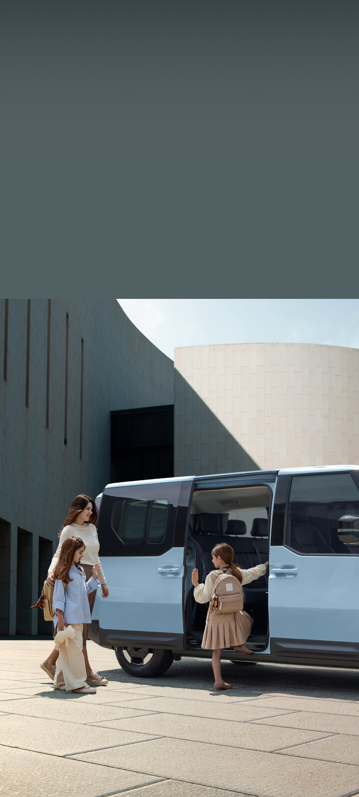 The Kia PV5 Passenger with dual sliding doors open, as a mother and children prepare to board