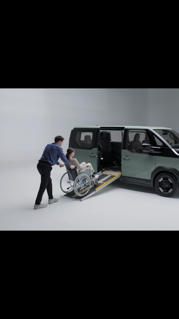Rollstuhlfahrer wird mithilfe einer eingebauten seitlichen Rampe in einen Kia PV5 WAV geholfen, die sich sauber unter dem Fahrzeugboden verstauen lässt.
