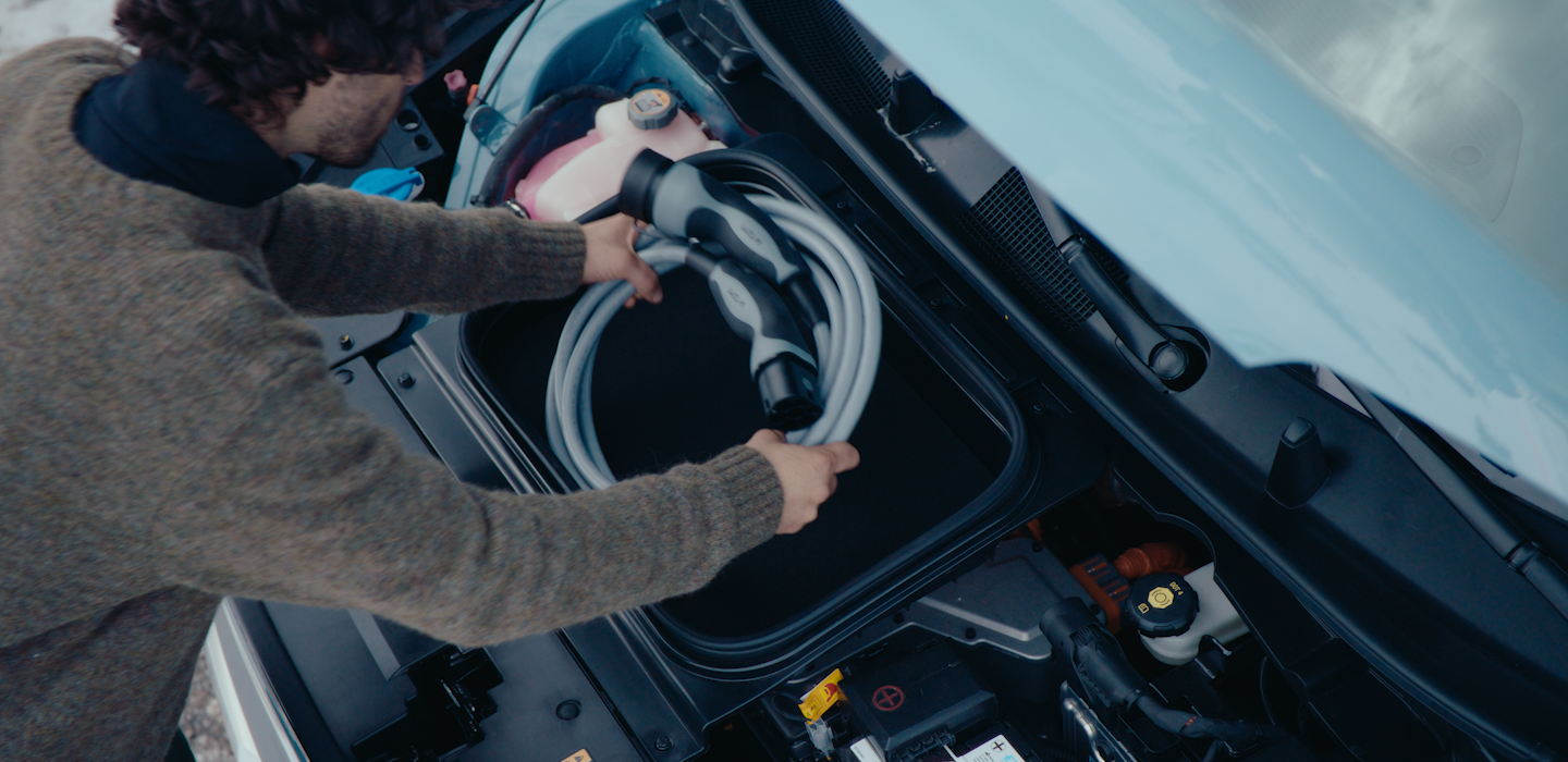 Close-up of a person removing a charging cable from its storage compartment under the hood of an electric Kia vehicle. 