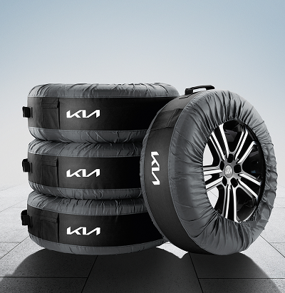 Three Kia-branded tyre storage bags stacked beside a fourth wheel with tyre encased in a matching protective bag.