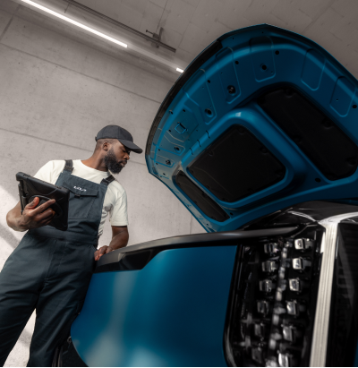 Close-up of a technician performing a vehicle safety check, measuring tread depth on a tire with a gauge during a workshop inspection.