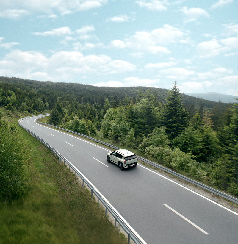 Kia EV3 circulando por un pintoresco camino forestal hacia el horizonte.