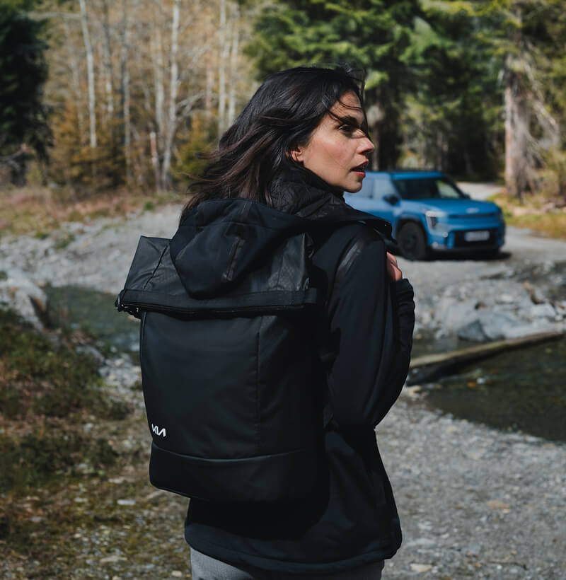 Una aventurera con equipo de la Kia Collection regresa a su Kia EV9 después de una caminata por la naturaleza.