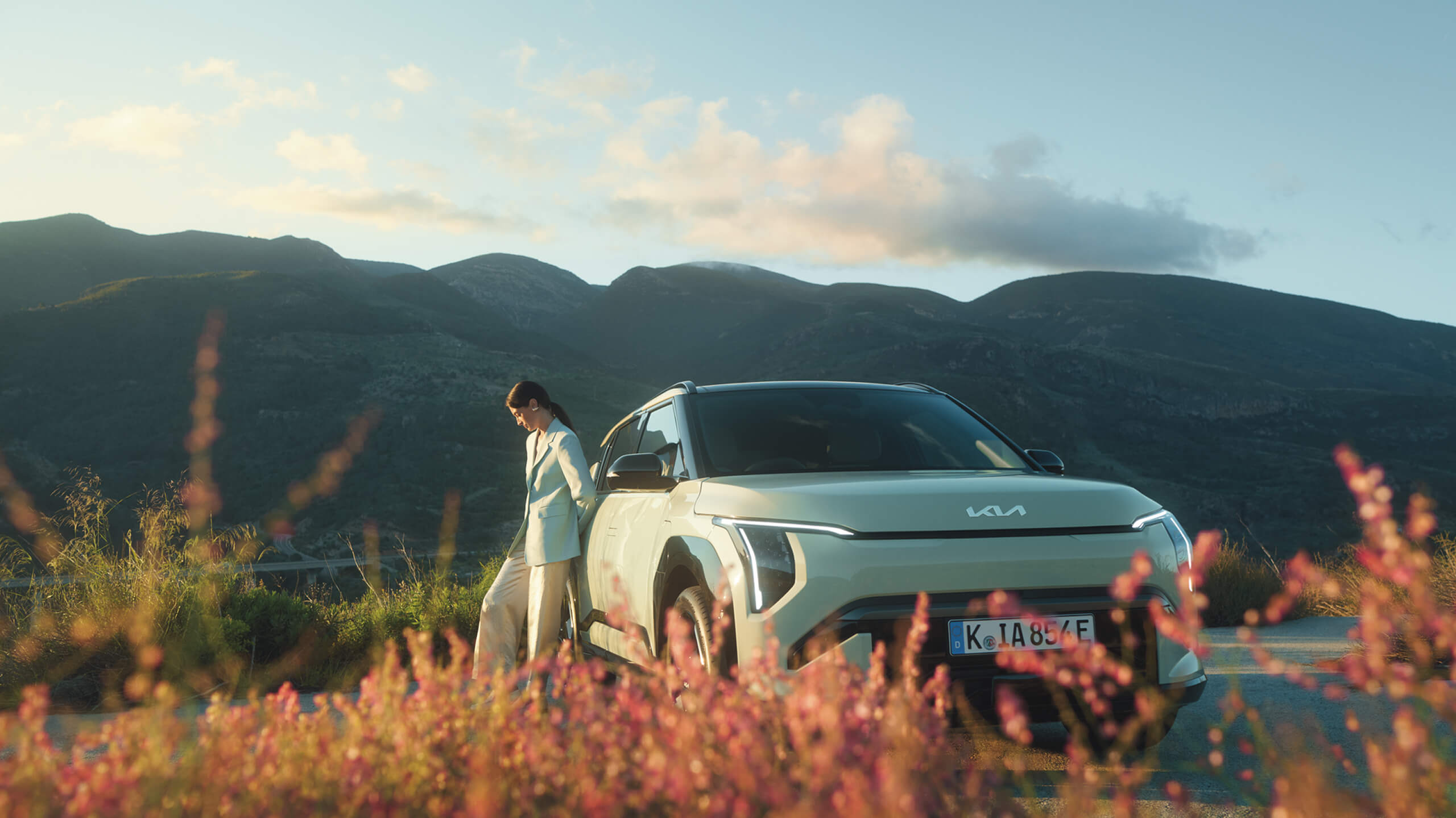 Eine Frau genießt den Sommer in einer wunderschönen Berglandschaft neben ihrem Kia EV3.