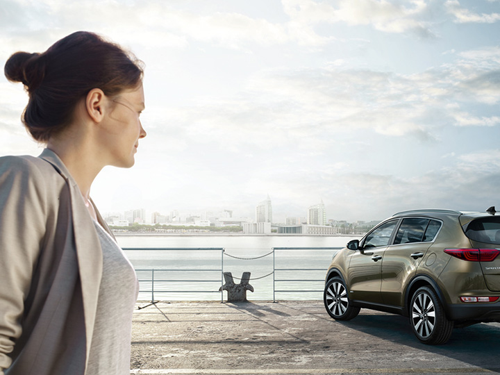 Woman looks to the car and the sea with a city in the background