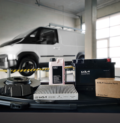 Kia Genuine Parts display in workshop with Kia PV5 elevated on heavy-duty lift in background.