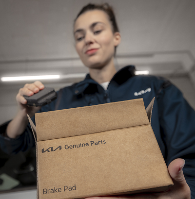 Kia technician unboxing Kia Genuine Brake Pads from a carton.