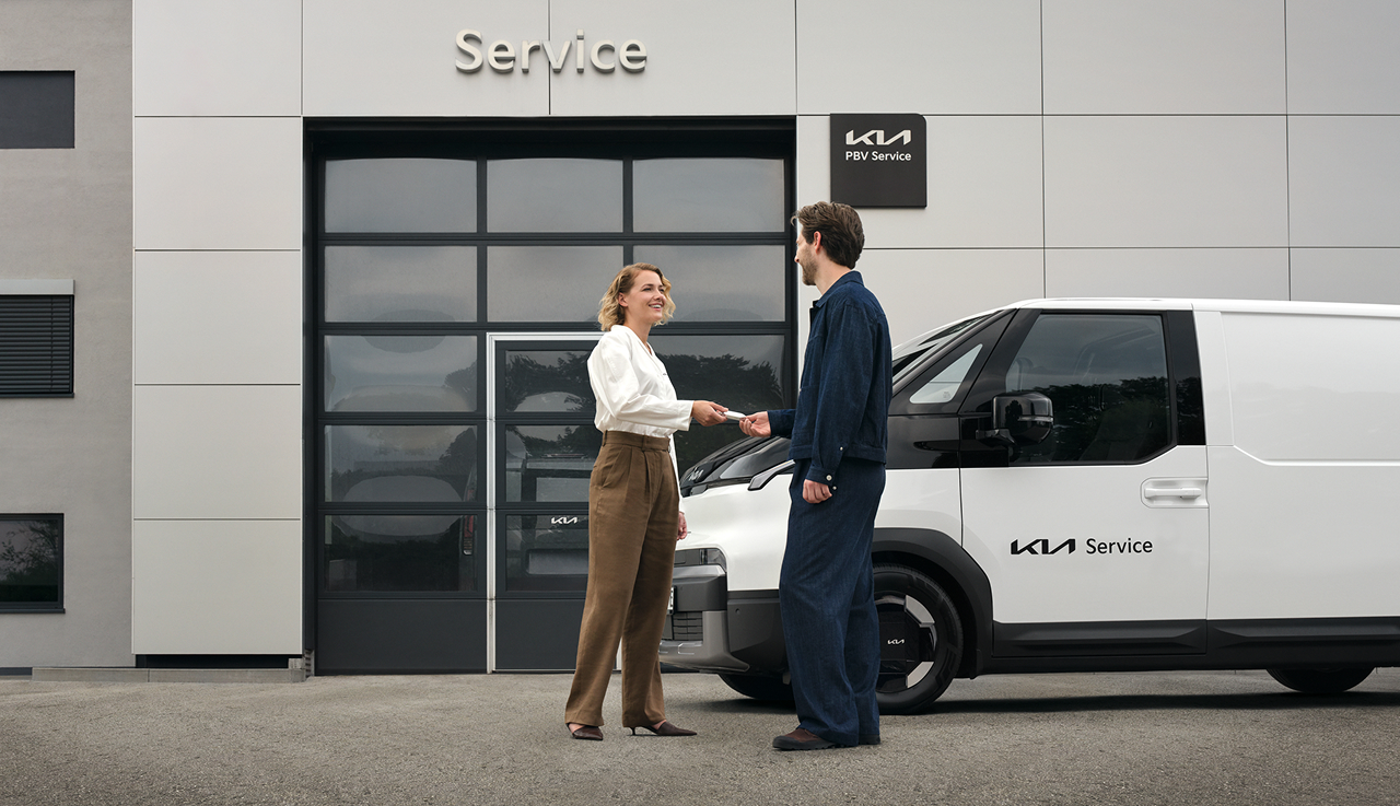 Young business owner picks up his white Kia PV5 with roof rack gallery in front of the Kia workshop.