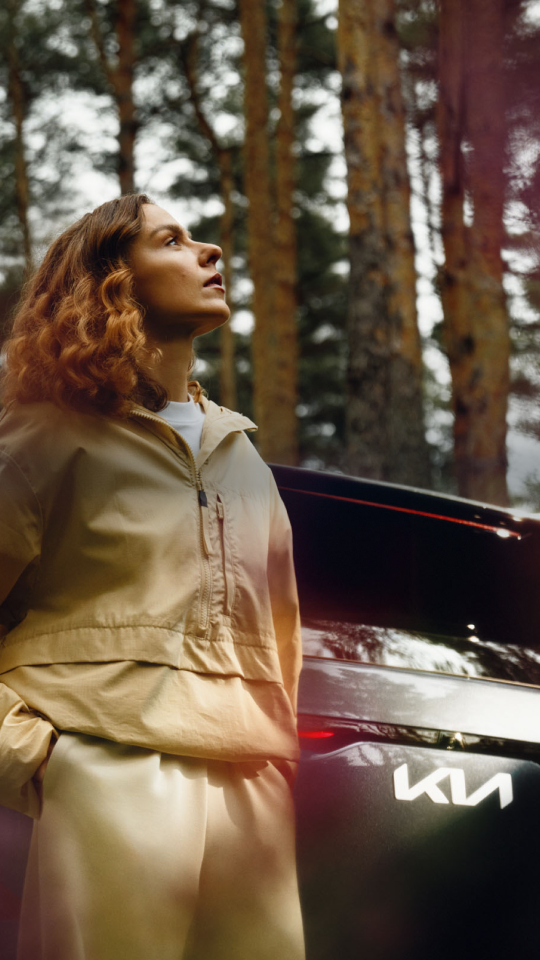 Woman enjoying the fresh summer air beside her Kia EV5.