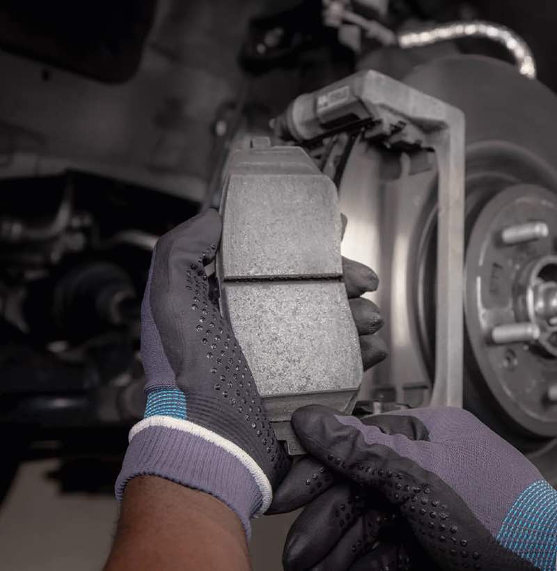 Technician is replacing worn brake pads and discs of an older Kia with Kia Genuine Parts.