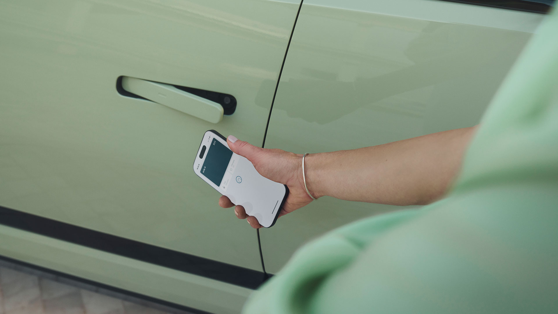 A person holds a cell phone beside a green Kia EV3, showcasing the digital key feature.