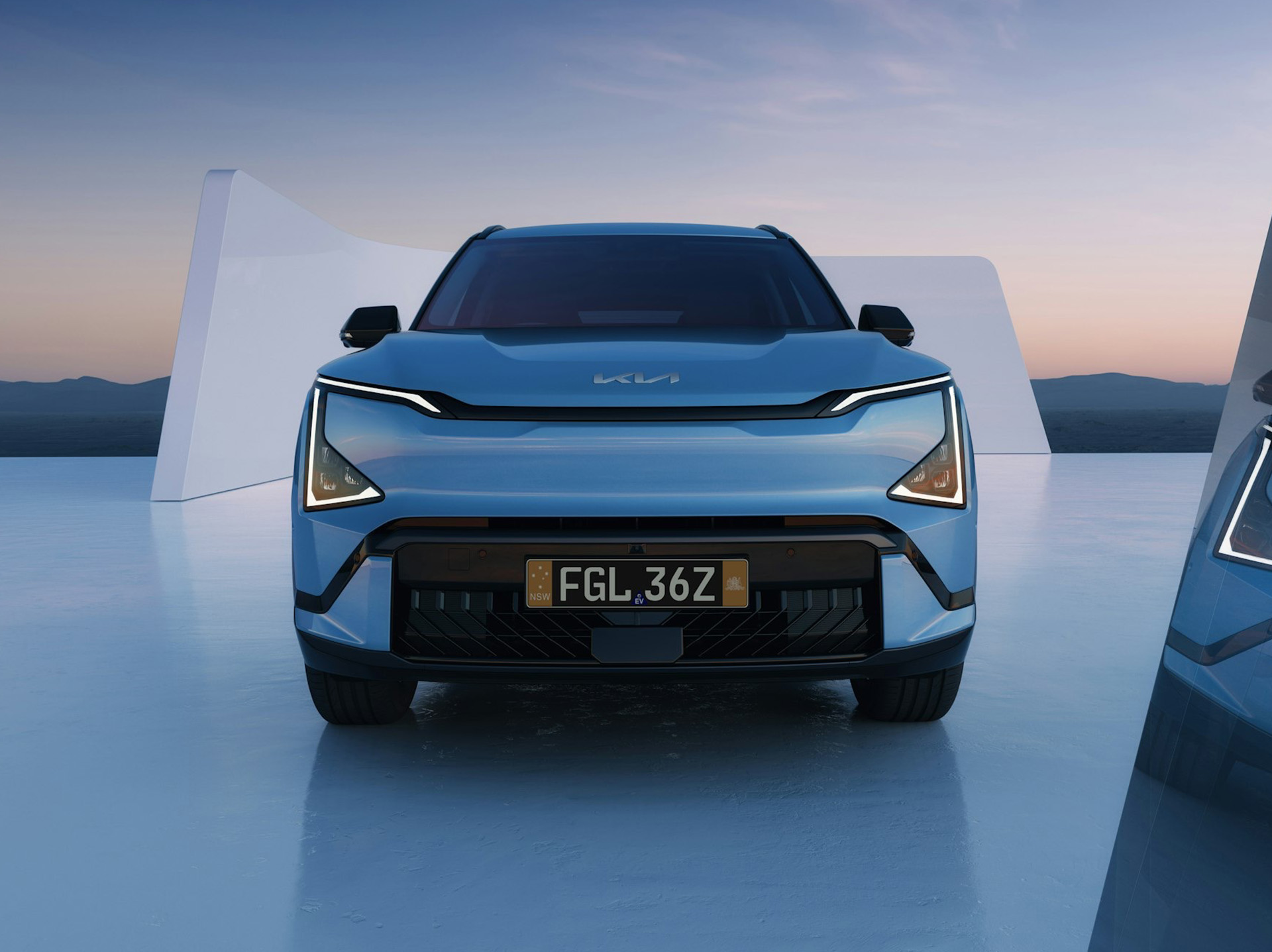 Front view of a Kia EV3 with a person standing beside it, in a scenic outdoor location.