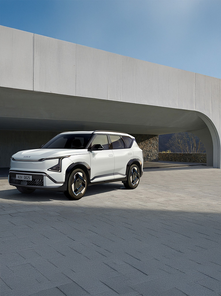 A person leans against a Kia EV3 charging at a station, set against a rocky mountainous background.