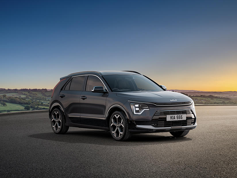 Black Kia Niro Hybrid parked on an open road with a scenic countryside backdrop at sunset