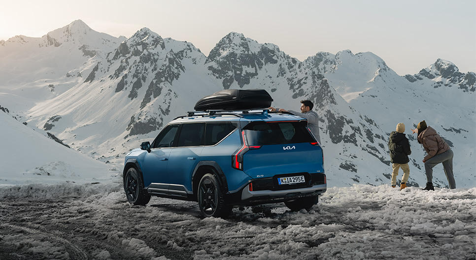 Kia EV9 on the side of a snowy cliff, with a family stood near by.