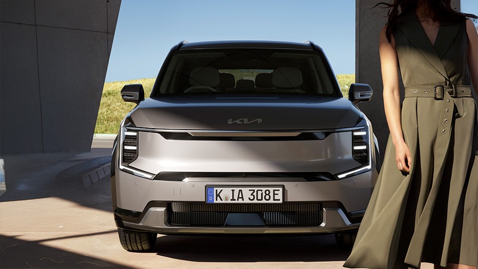 The Kia Sortento ‘4’ in Interstellar Grey positioned in front of a wooden structure, with a lady stood next to the opened passenger door.