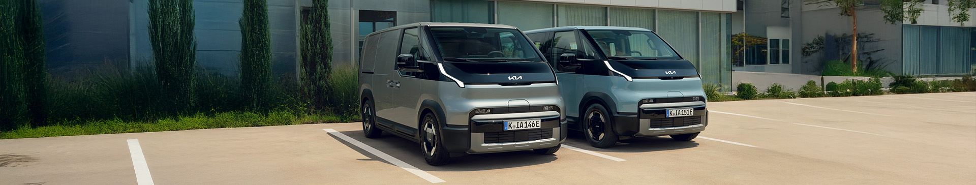 A side profile of the Kia GT-Line S EV6 in Wolf Grey, with a man sat in the passenger seat his legs out of the car. The EV is parked in an area with stones on the floor, and cylindrical cooper panelled building behind.