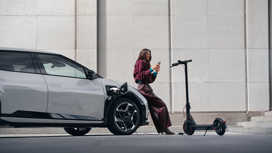 The Kia EV4 in Wolf Grey charging a scooter